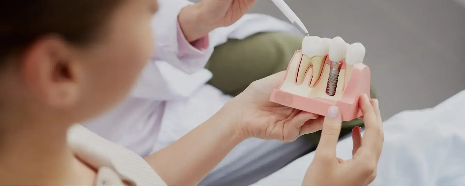 Dentist showing patient dental implant model with crown and titanium post fixture.