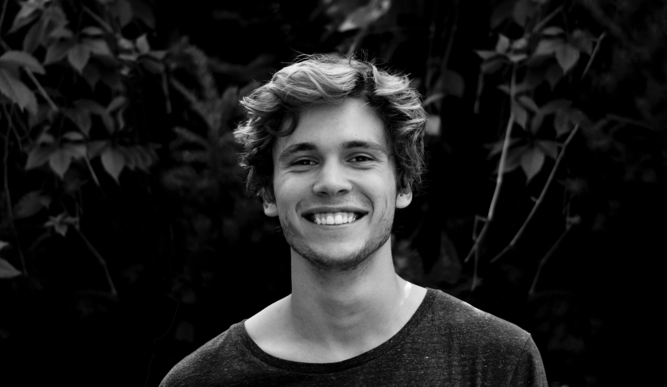 Young man with a bright smile against a leafy background, representing a satisfied dental patient.