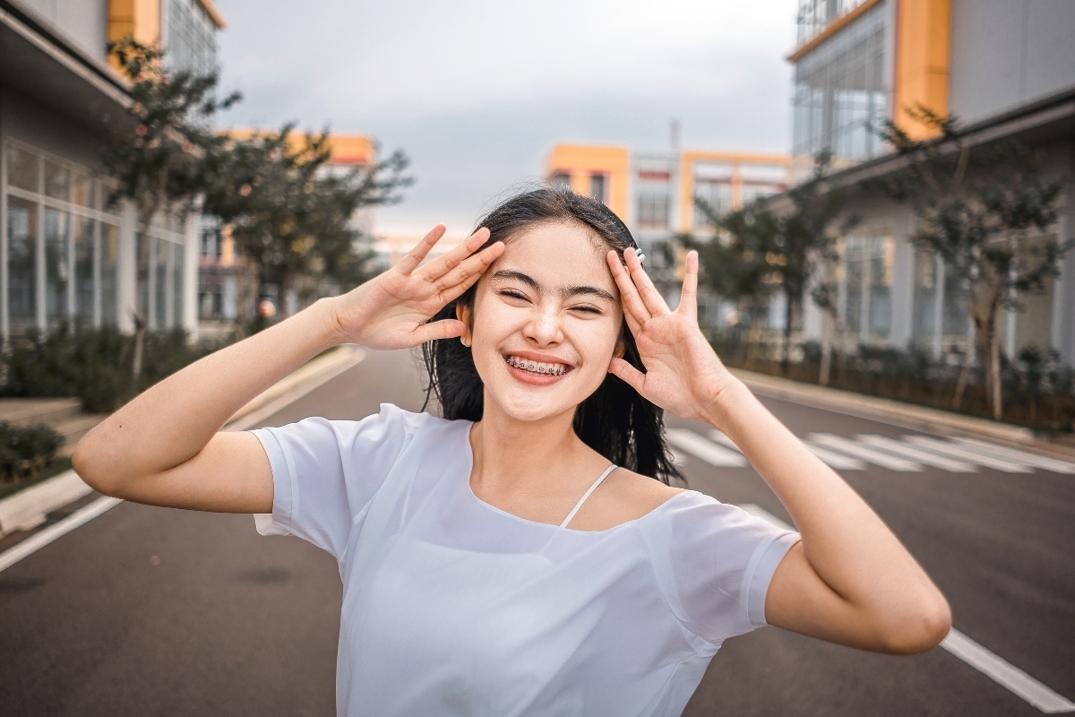 Young woman with braces smiling confidently outdoors on a residential street.