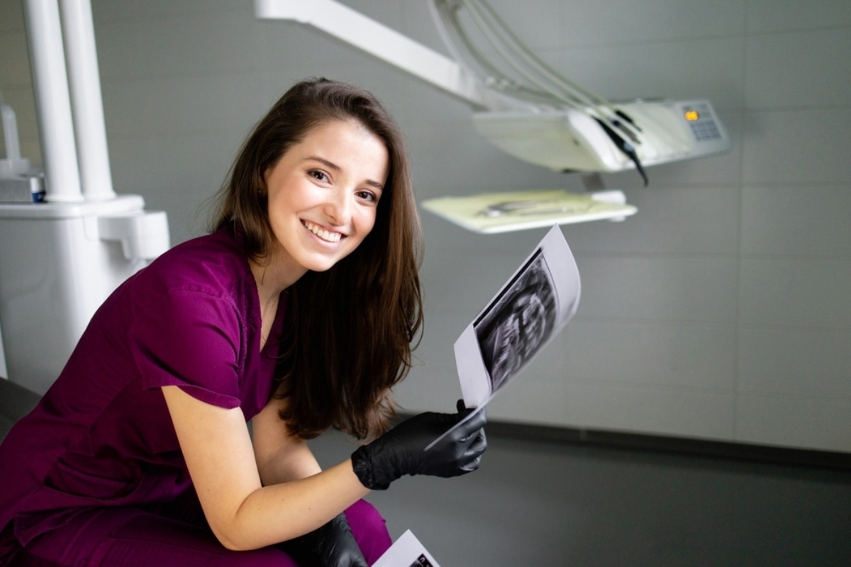 Dental hygienist holding X-ray images in treatment room with overhead light.