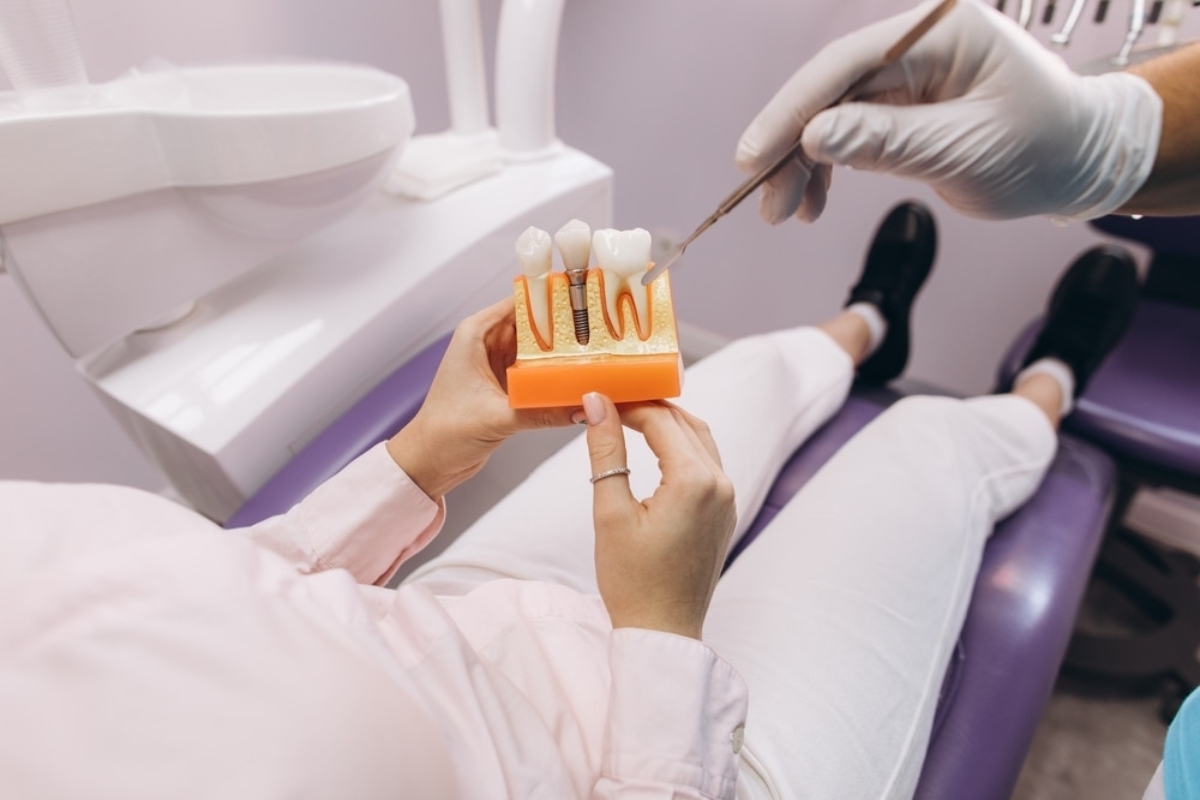 Dentist pointing to dental implant model showing tooth replacement procedure with patient in treatment chair.