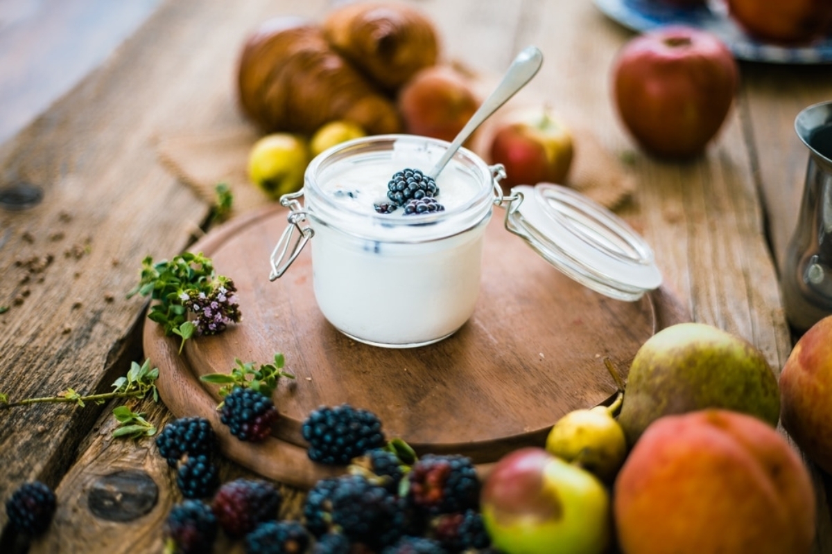 Creamy yogurt with blackberries surrounded by fresh fruits, supporting dental implant health through calcium and protein.
