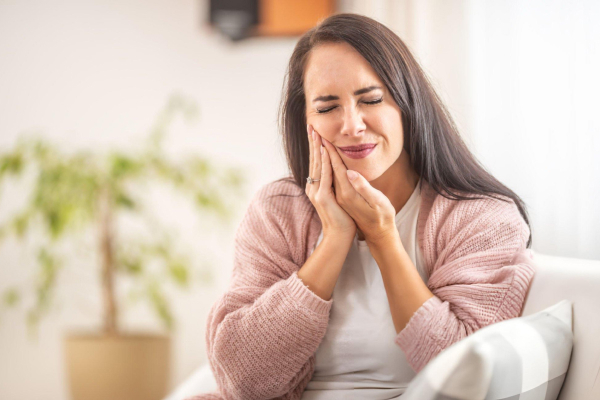 Woman holding her cheek in pain, experiencing dental discomfort requiring emergency care.