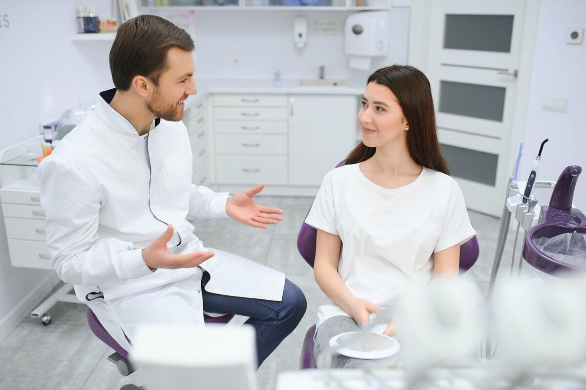 Male dentist consulting with female patient in modern dental office treatment room.