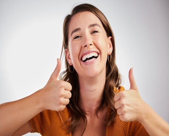 Woman smiling with thumbs up, showing confident results from cosmetic dentistry.
