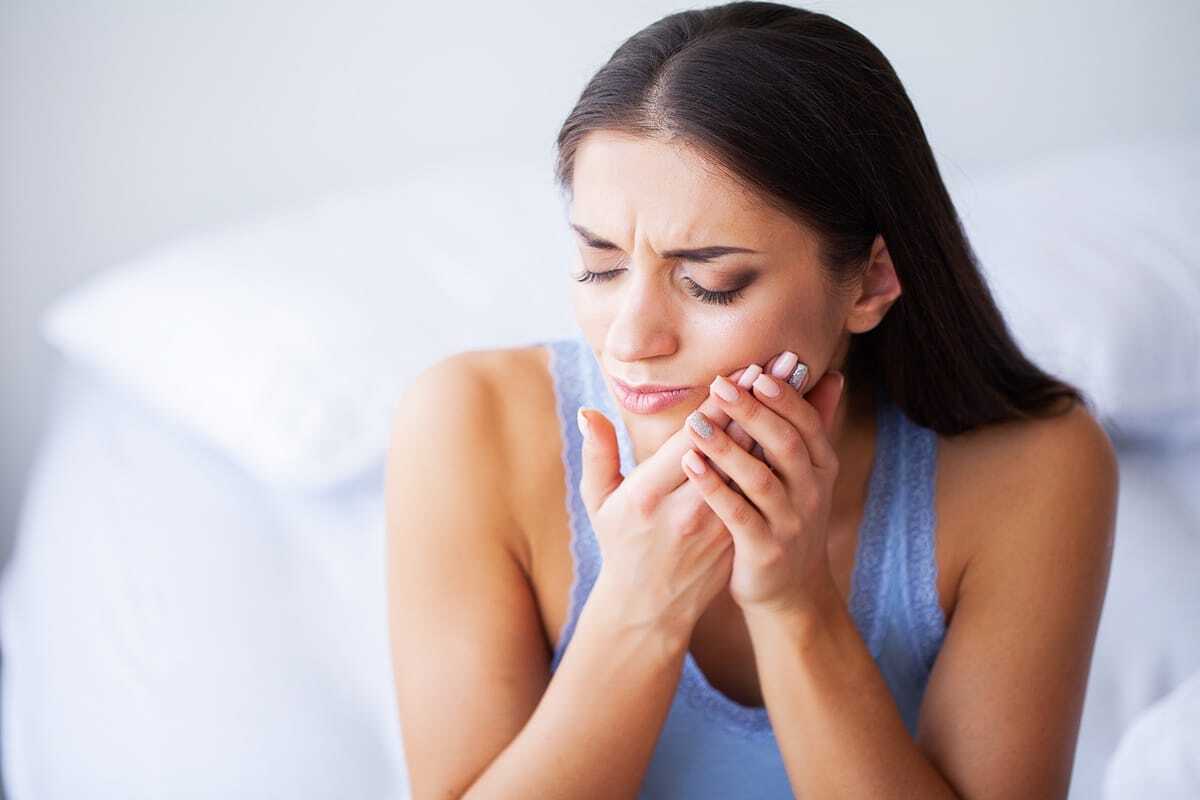 Woman experiencing tooth pain, holding her cheek in discomfort.