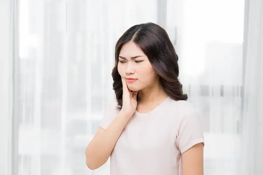 Woman in dental office holding her cheek, appearing to experience tooth pain or discomfort.