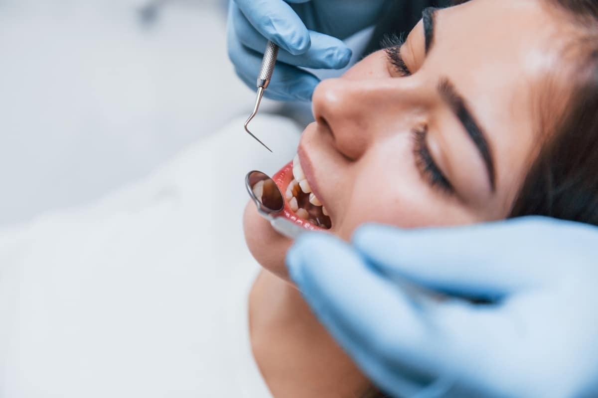 Dentist examining patient's teeth with dental mirror during same-day appointment.