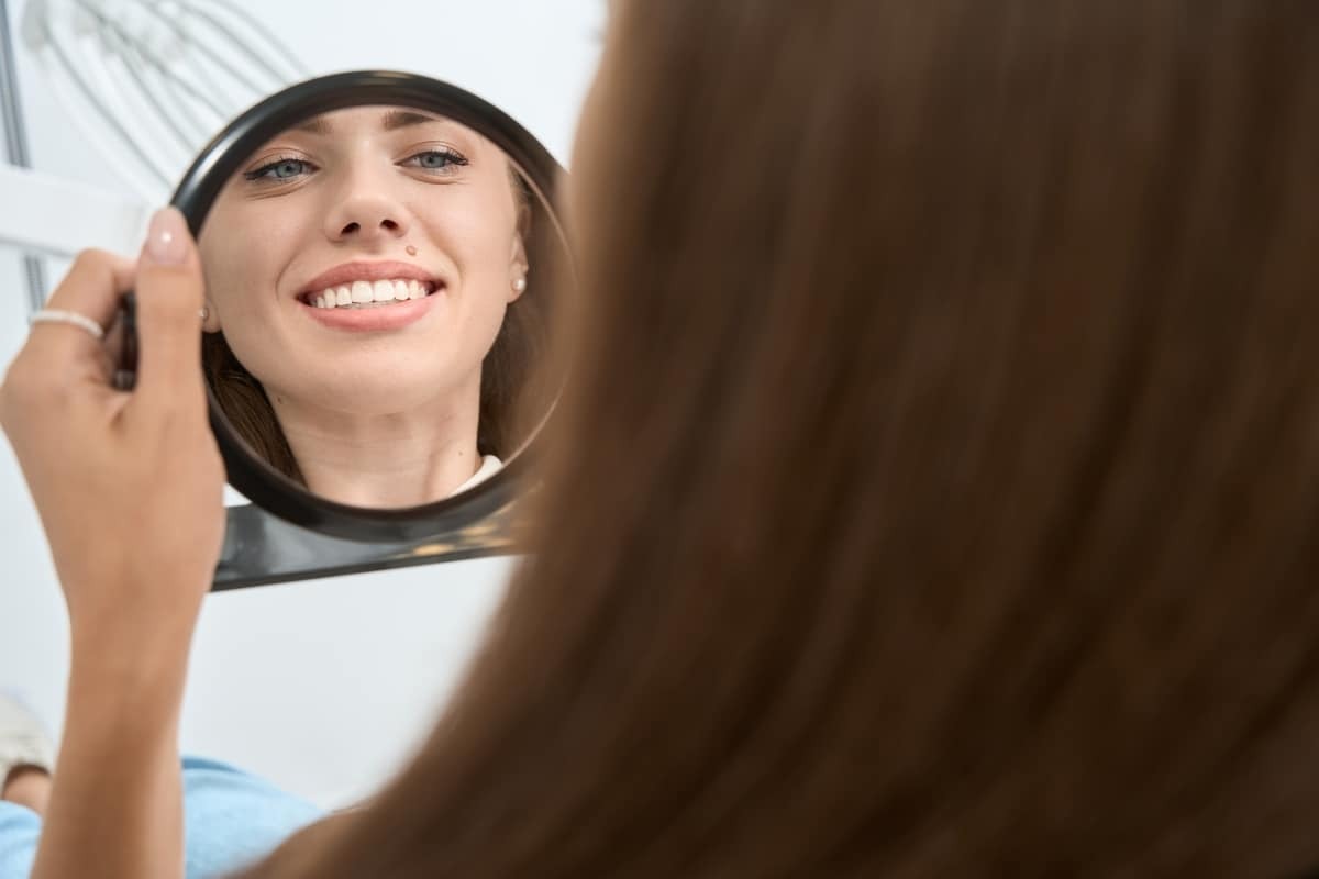 Woman smiling at her reflection in a mirror, showing confident teeth after cosmetic dental treatment.