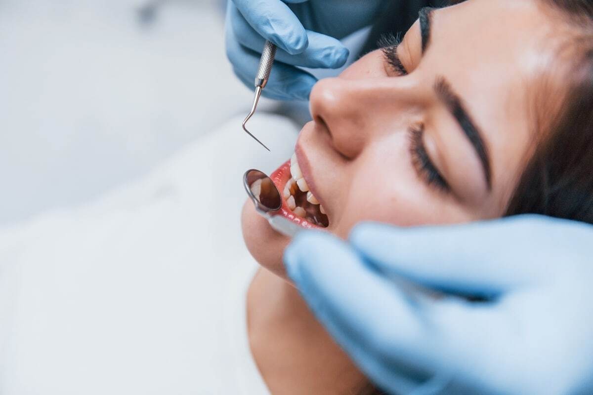 Dentist examining patient's teeth with dental mirror during routine oral exam.